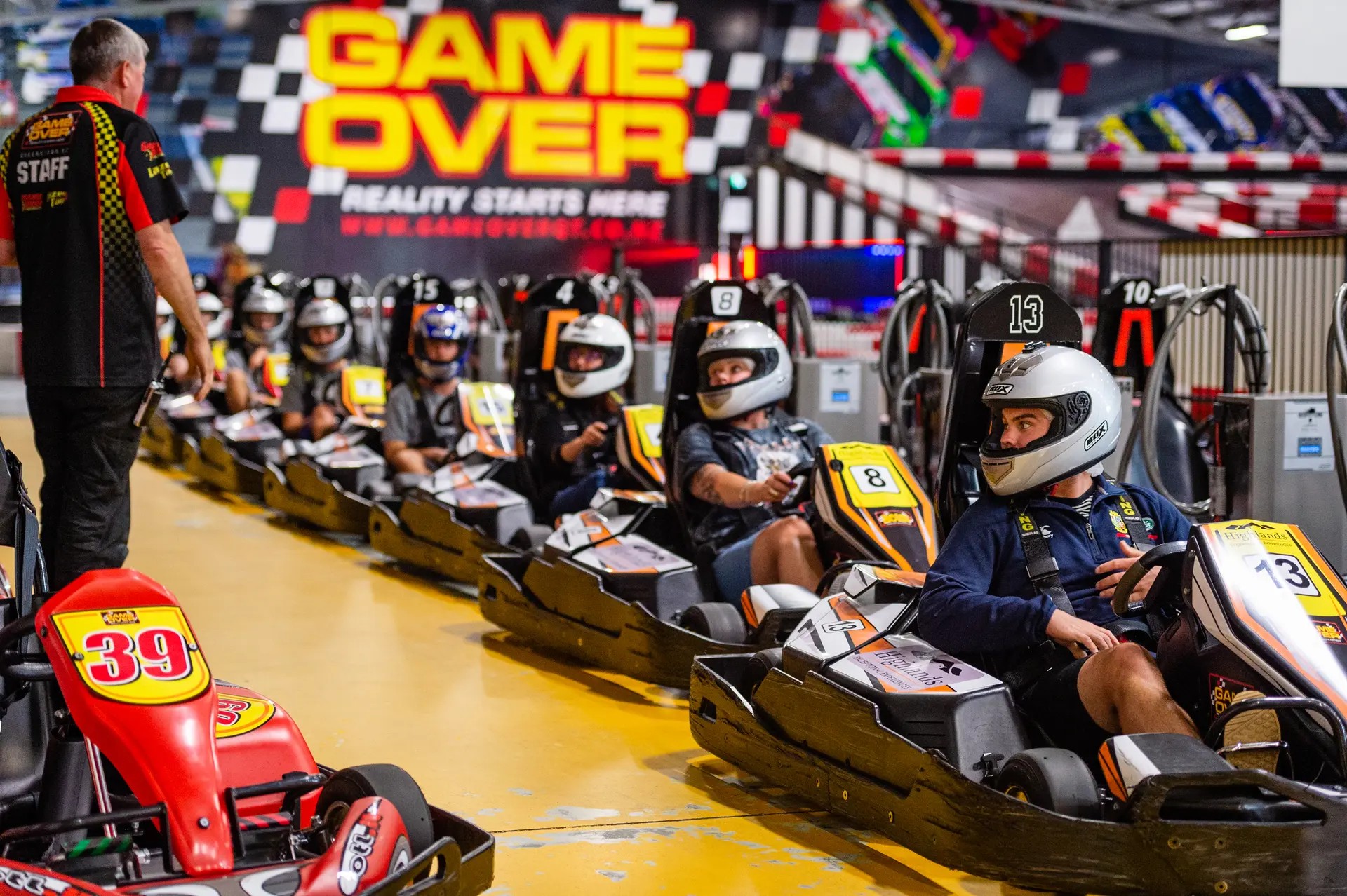 Kids wearing helmets in go karts at the start of an indoor track.