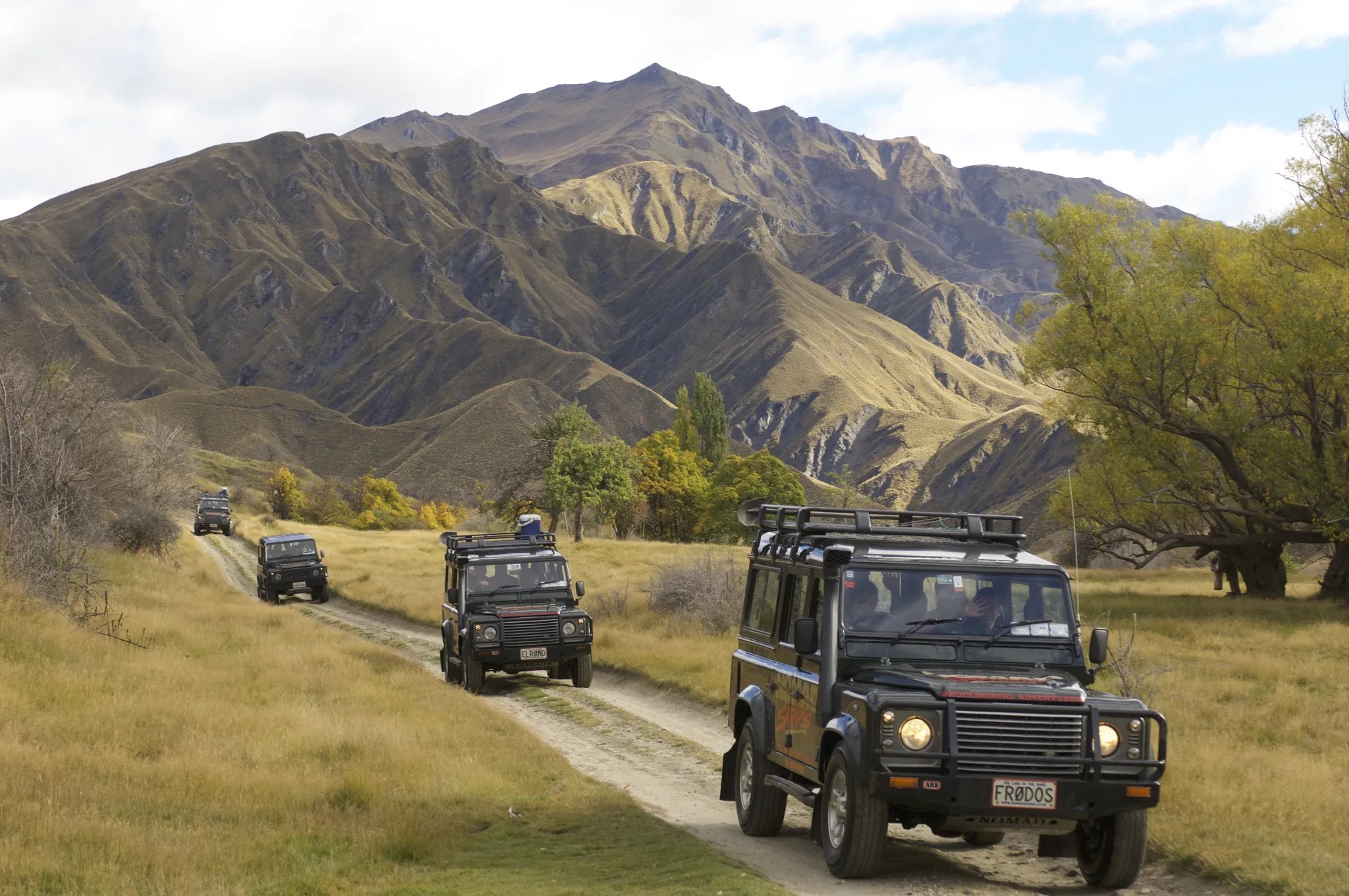 Three offroad cars on a trail in a field with mountains in the background.