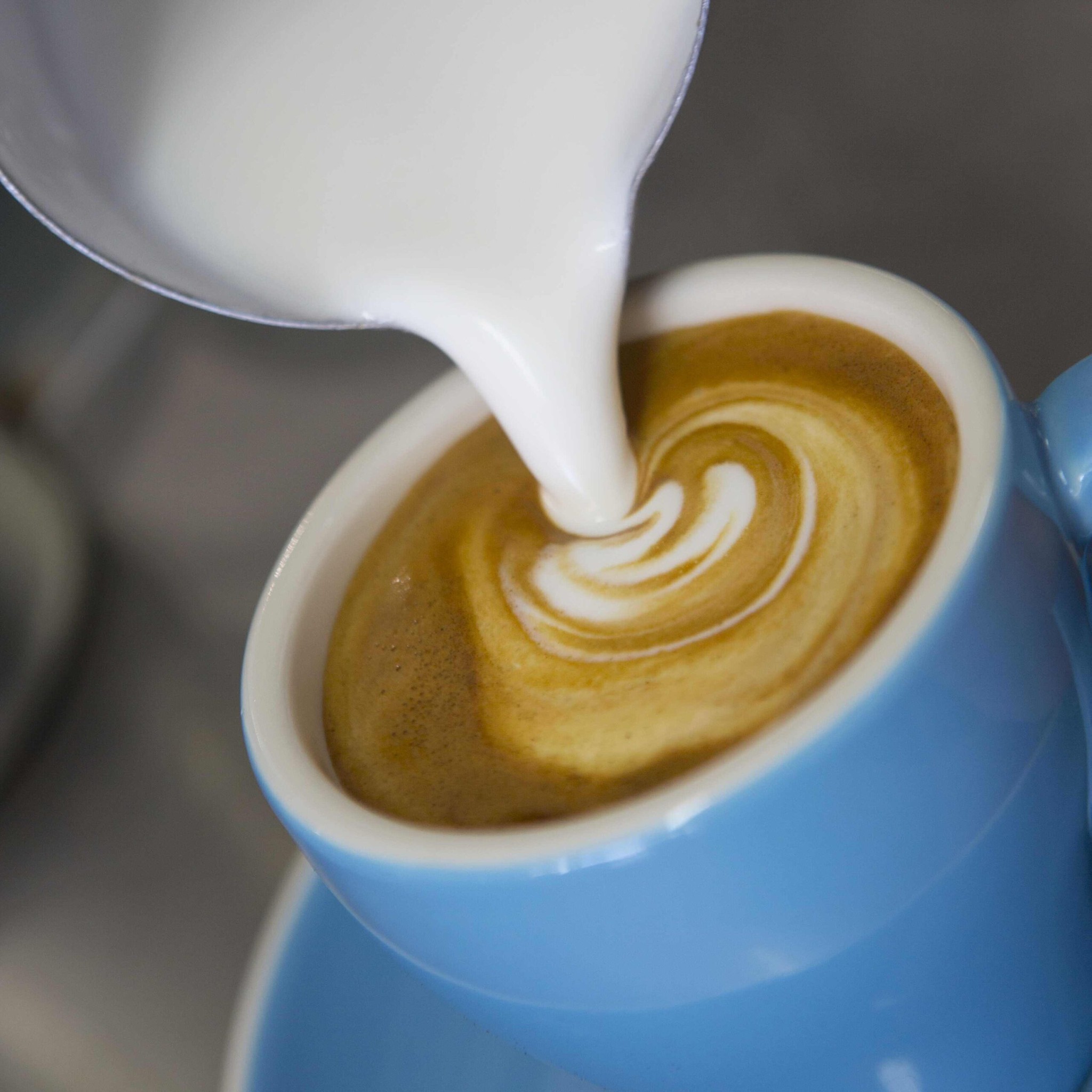 A latte being poured into a blue mug.