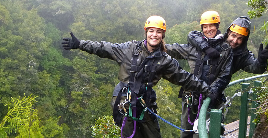 Three adults enjoying a suspended bridge in the rain at Canopy tours