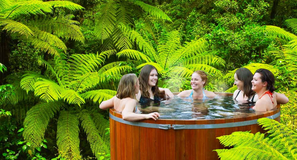 A group of friends enjoy the cedar hot tubs surrounded by lush forest at Secret Spot Hot Tubs in Rotorua.