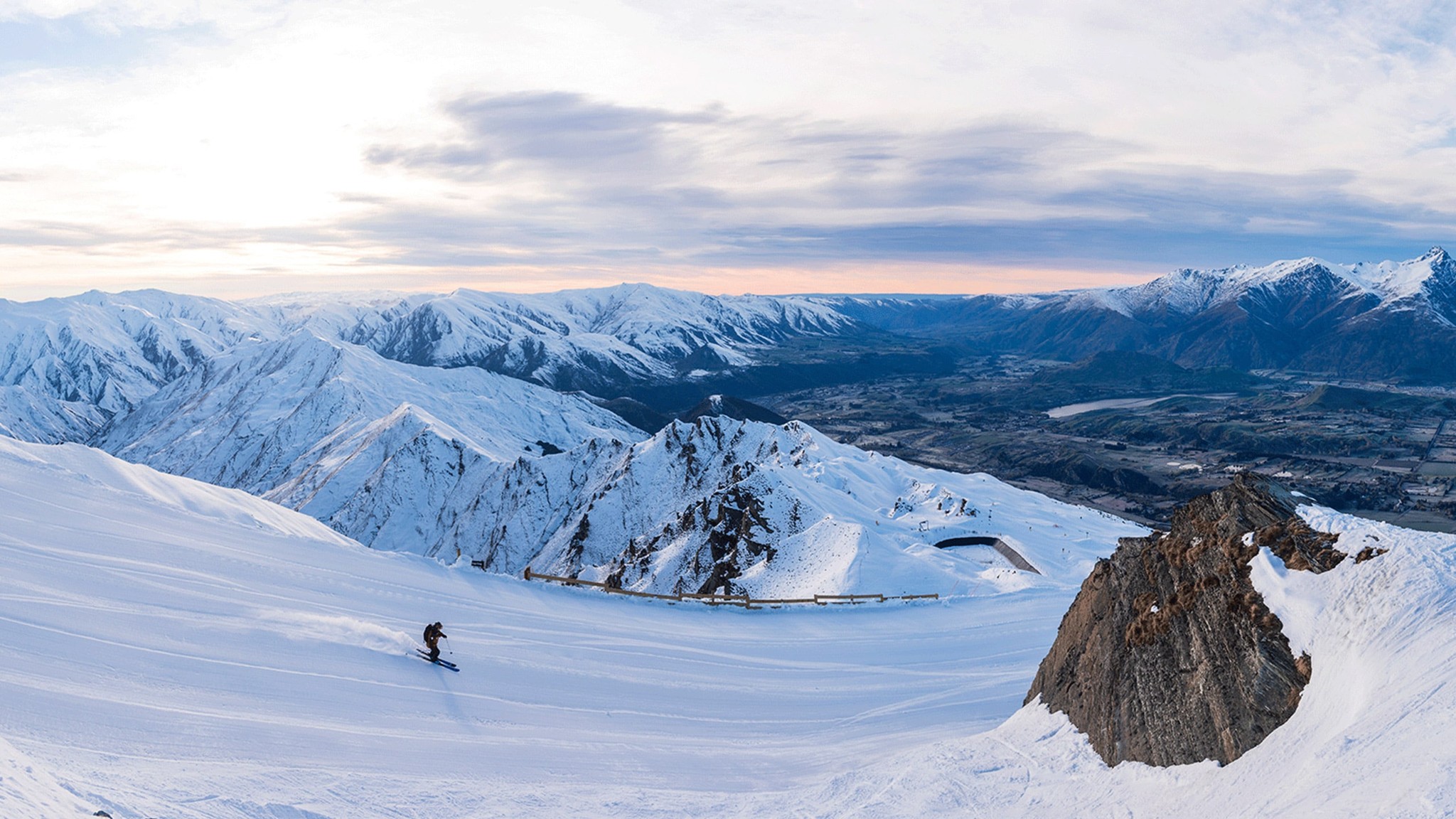 A skier make their way down a ski slope with mountains stretching into the distance.