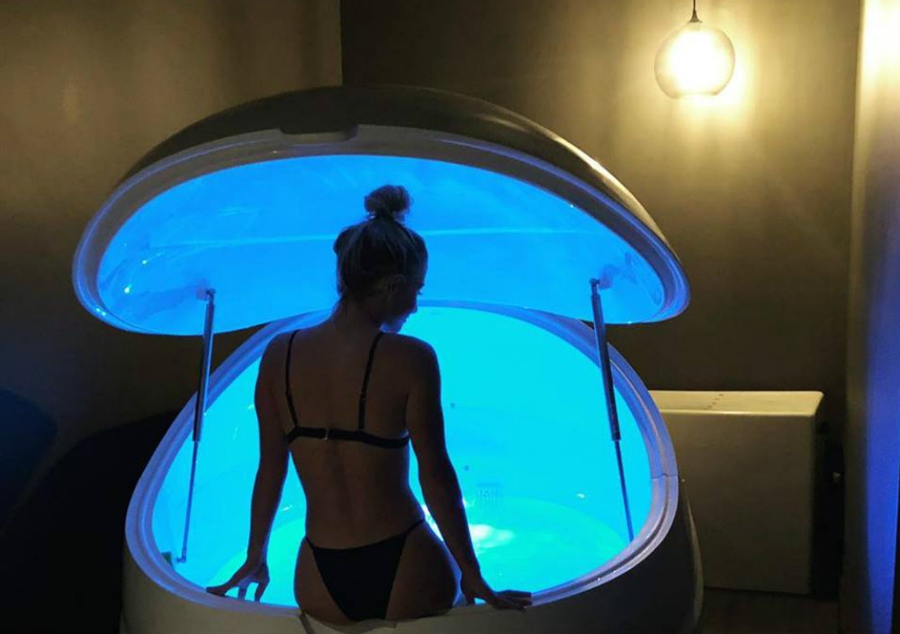A woman sits on the edge of a glowing salt spa capsule.