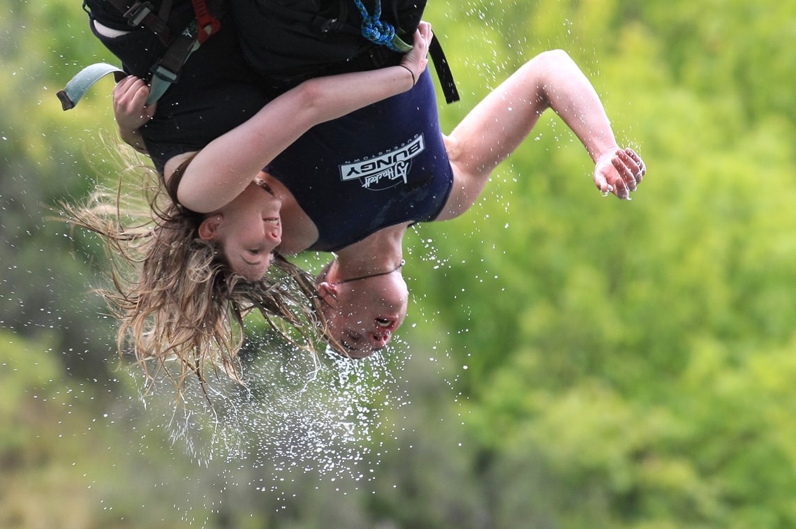 Water drips from two bungy jumpers on their rebound during their jump.