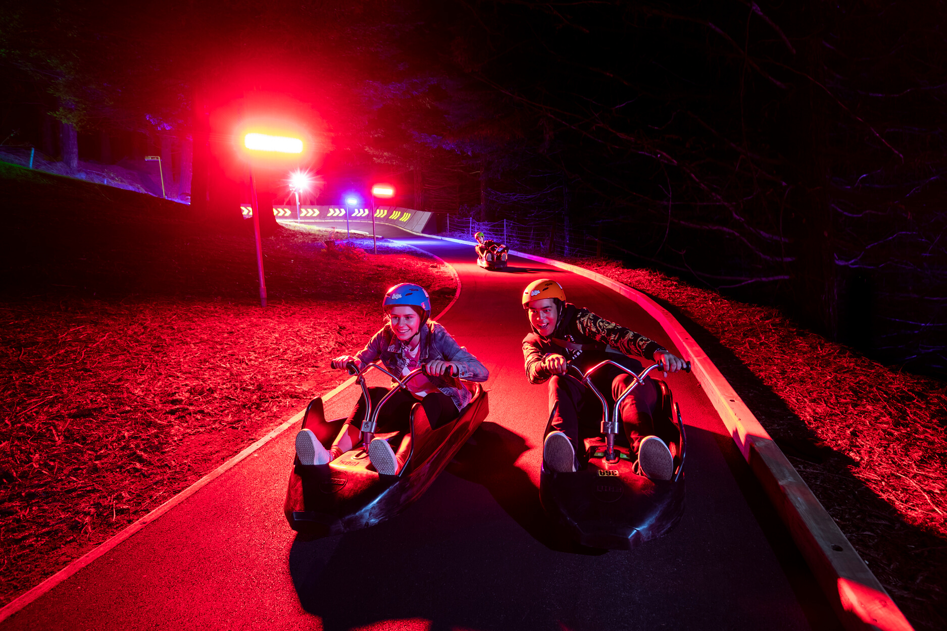 Two friends smile as they race each other down the Skyline Rotorua Night Luge tracks.
