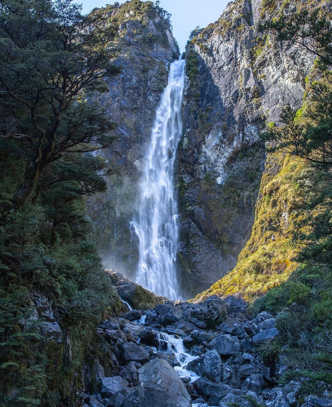 A towering waterfall with cascading waters running down located in the Arthurs Pass.