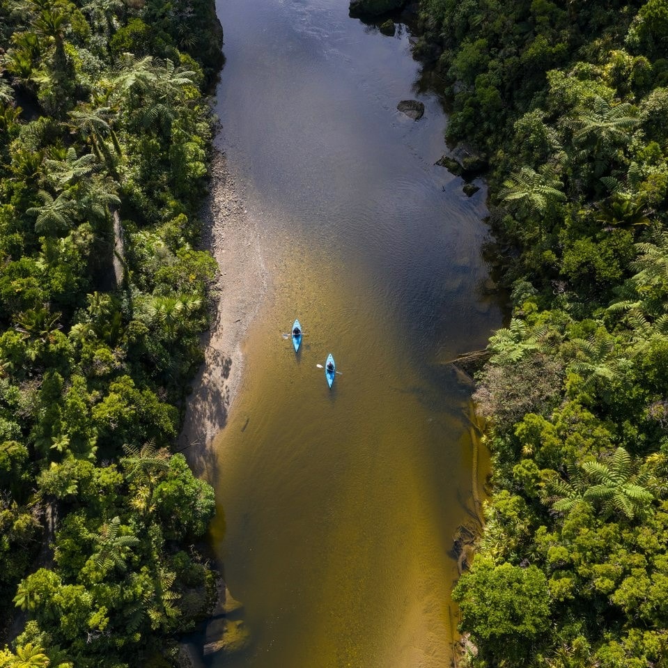 Two kayakers meander down a bush clad river on the West Coast of New Zealand.