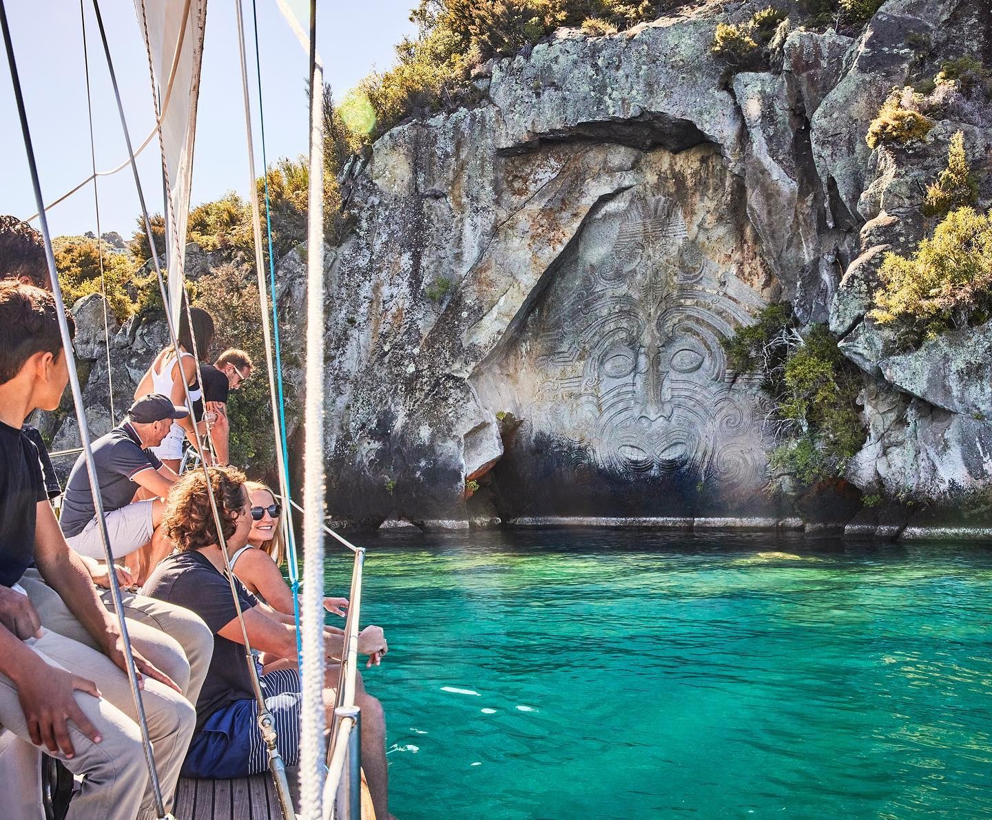 A group of people enjoy Mine Bay Maori Rock Carving on Lake Taupo.