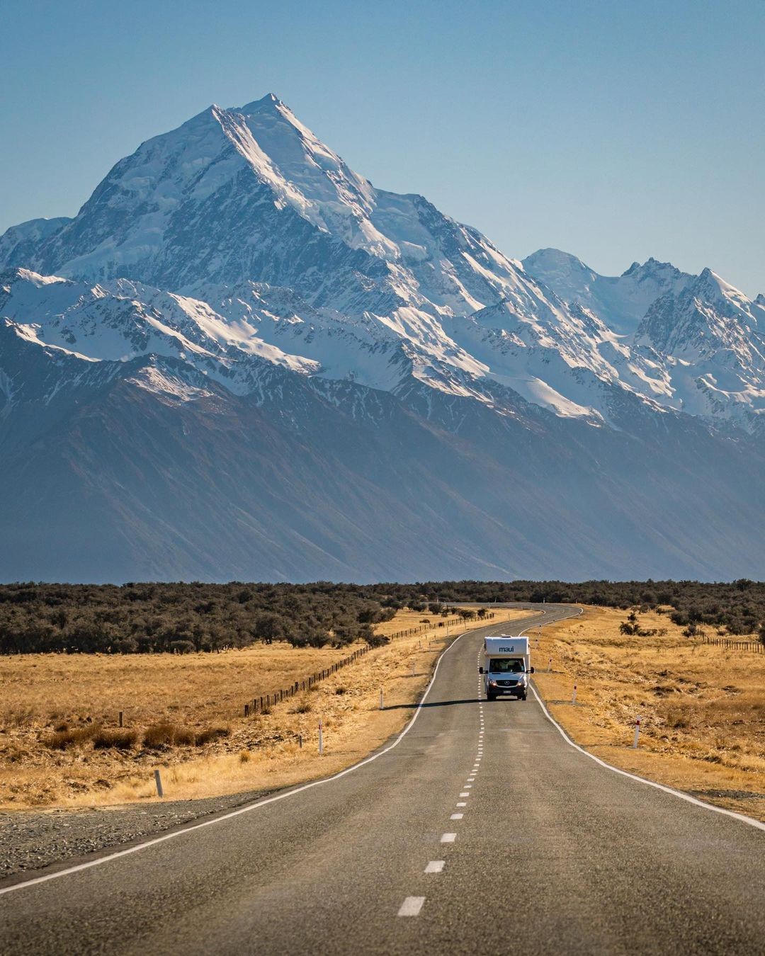 A campervan driving along with Mount Cook behind.