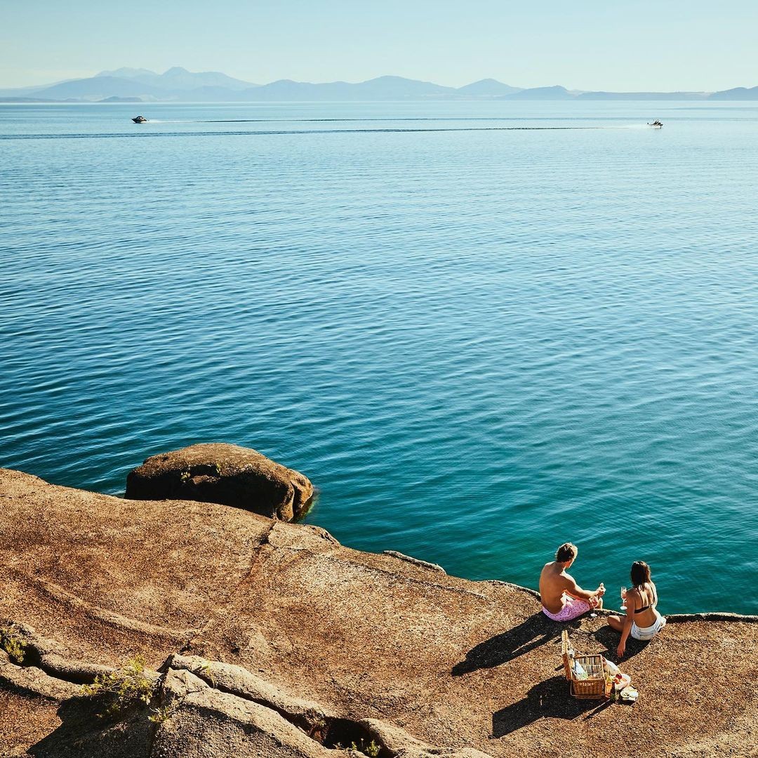 A couple relaxes by the Taupo lakeside with a picnic.