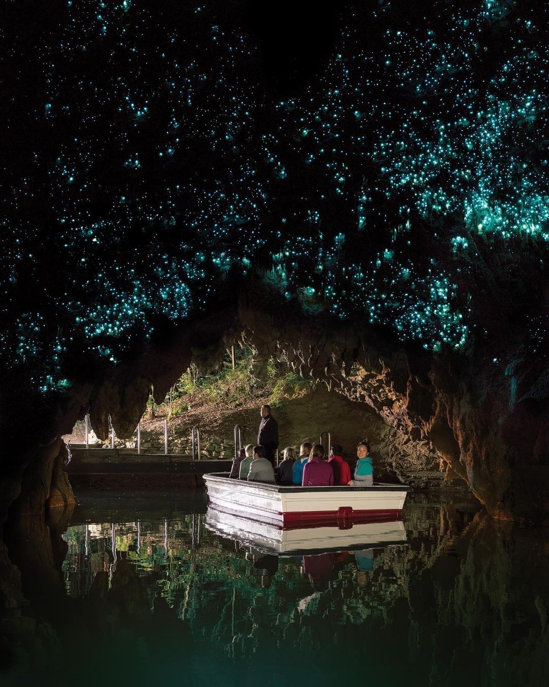 A group of people ride a boat through the Waitomo caves with glow worms on the roof.