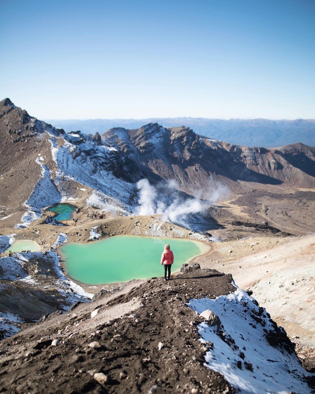 A lady stops to appreciate a steaming geothermal lake in the Tongariro National park.