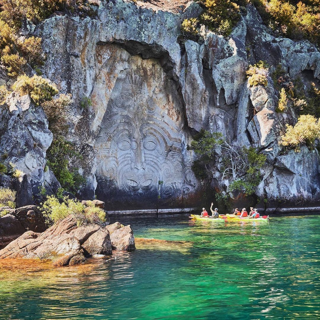Kayakers stop to appreciate the Ngatoroirangi Mine Bay Maori Rock Carvings on Lake Taupo.