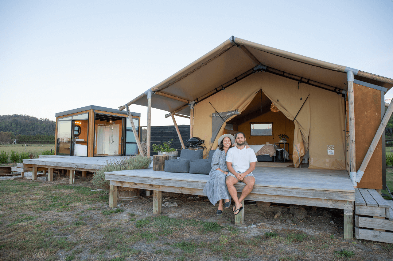 A couple sits on the deck of their glamping tent at Luxury Escapes in the Coromandel.