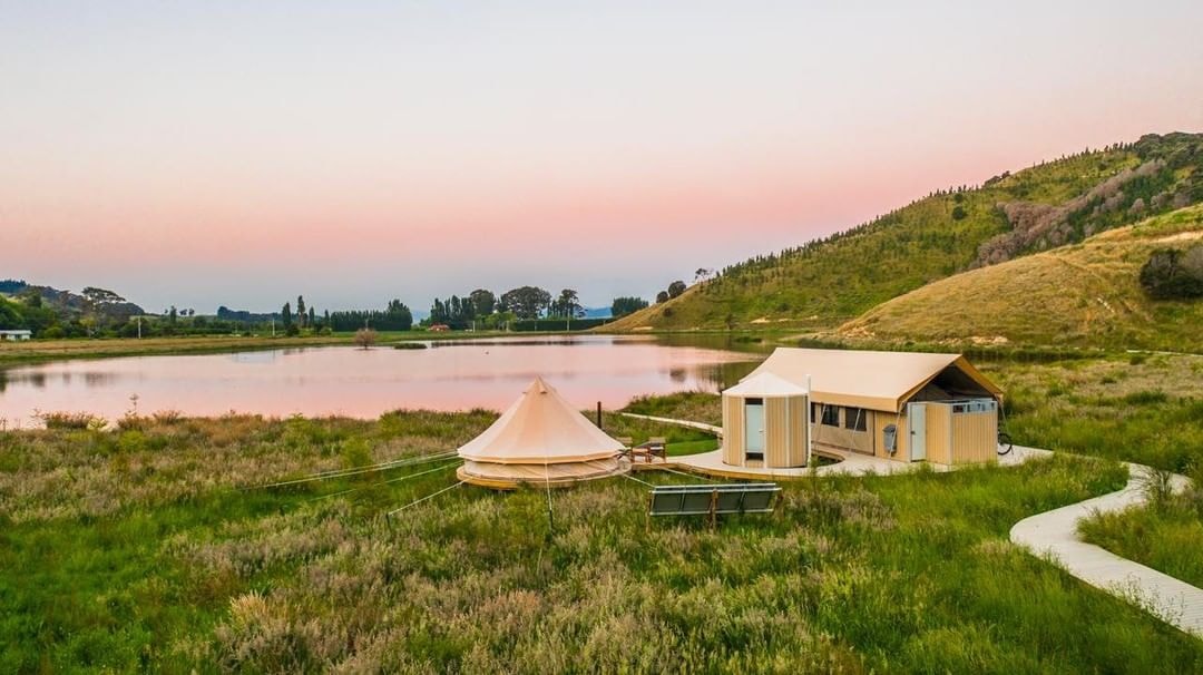 The luxurious Manutuke Eco Retreat positioned in front of a small pond with a sunset reflecting off it.