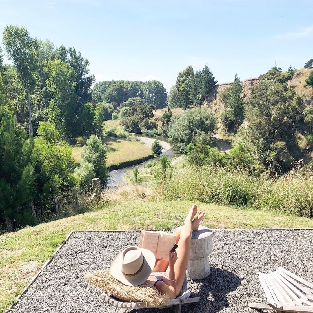 A woman reads a book at Clifton Glamping with views of a meandering river in the background.