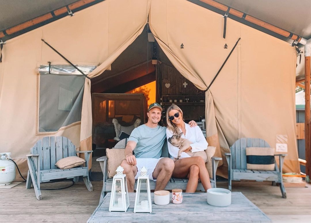 A woman and man sit outside their glamping tent with their dog at Waipu Glamping Getaway in Northland.