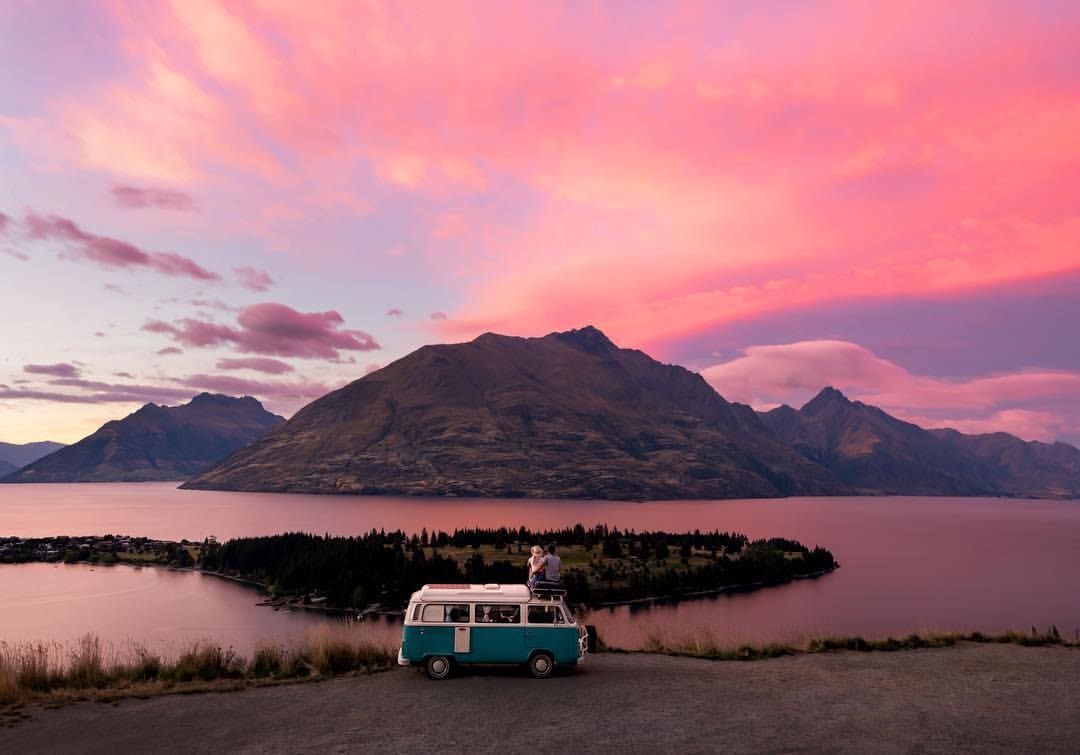 A couple sit on top of their campervan and watch a sunset from Queenstown Hill.