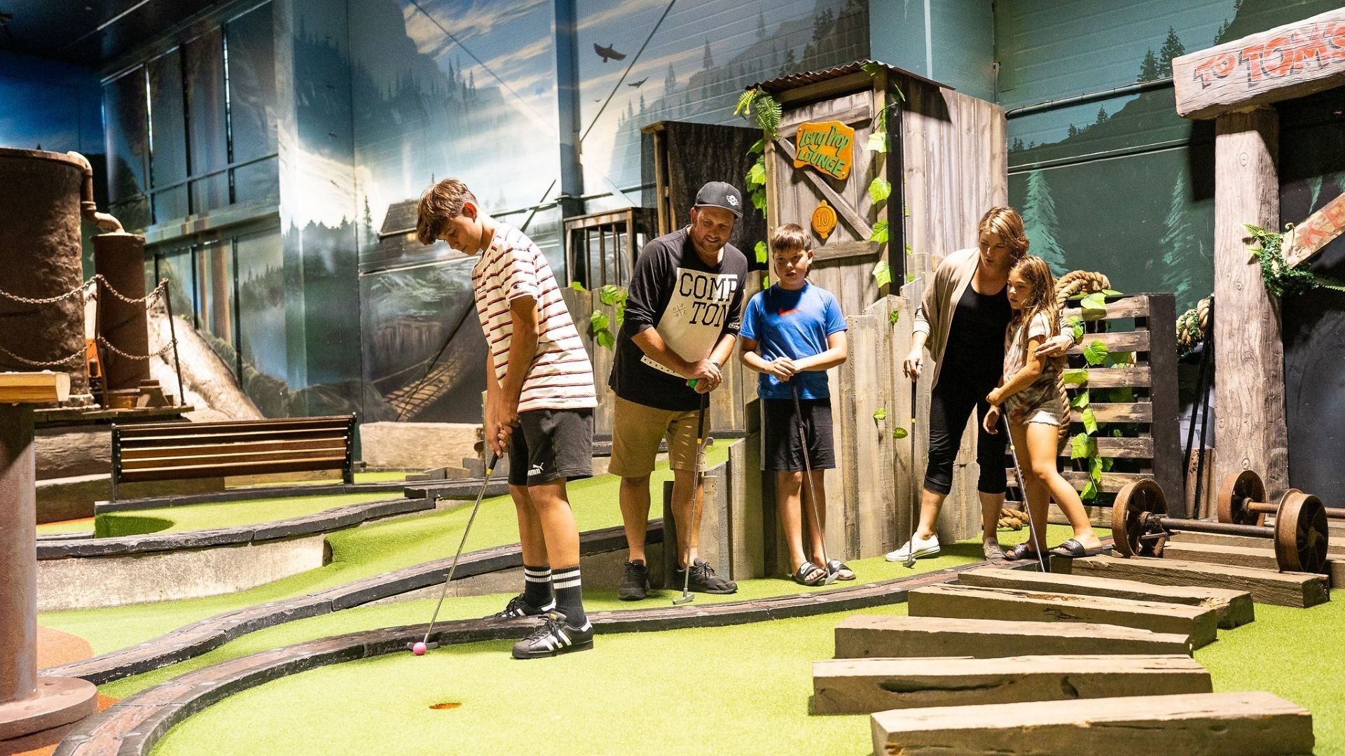 A family watches as their oldest son makes a putt for the hole at Lumberjax Mini Golf Rotorua.