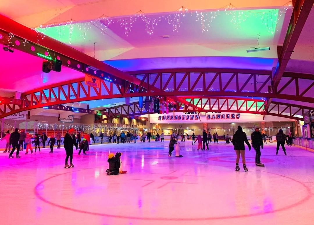 A group of people ice skate around under colourful lights at the Queenstown Ice Arena.