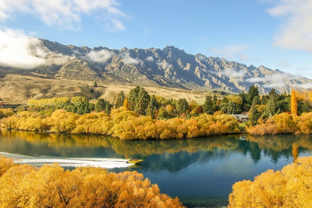 A jet boat speeds along the Kawarau river with stunning autumn colours behind.