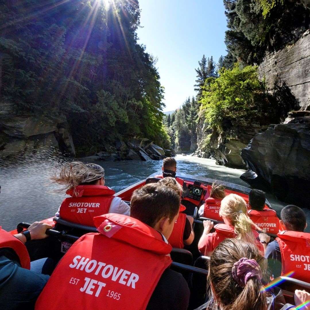 A Shotover Jet boat speeds through a narrow section on the river with customers holding on.
