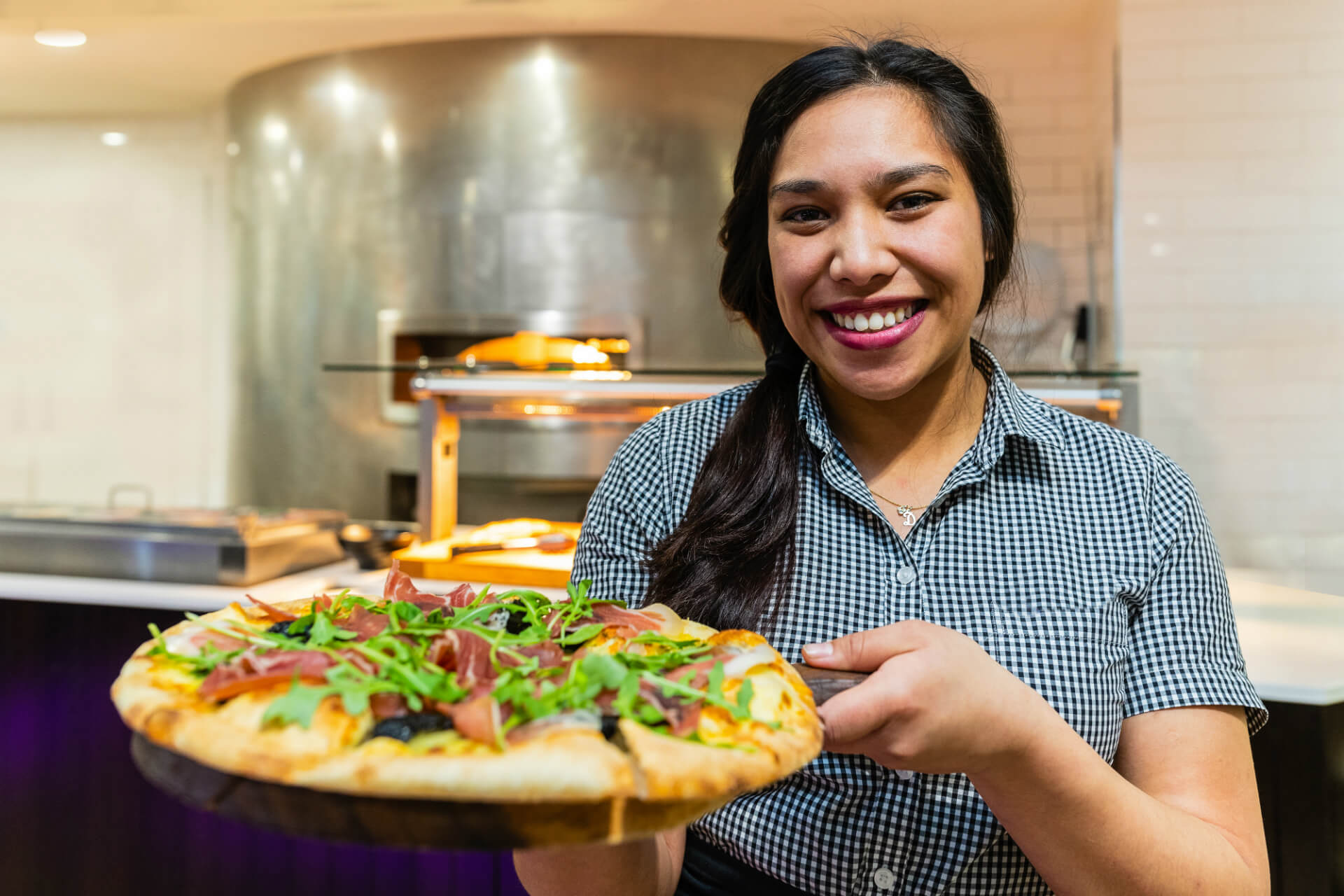 A Skyline Queenstown Employee presenting a fresh Italian pizza in front of the pizza oven.