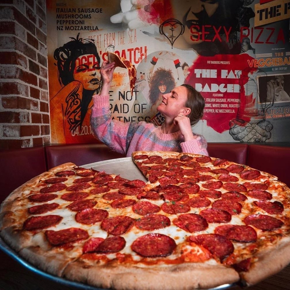 A woman stares at a slice of pizza the size of her head at Fat Badgers Pizza Queenstown ready to eat it.