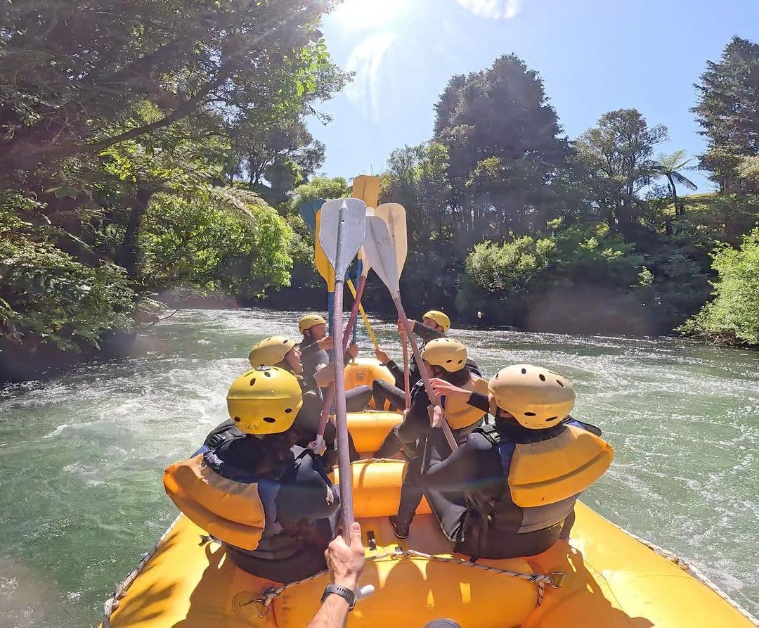 A group of customer on a Rotorua Rafting trip on the Kaituna River join paddles in the middle to celebrate navigating down a section of rapids.