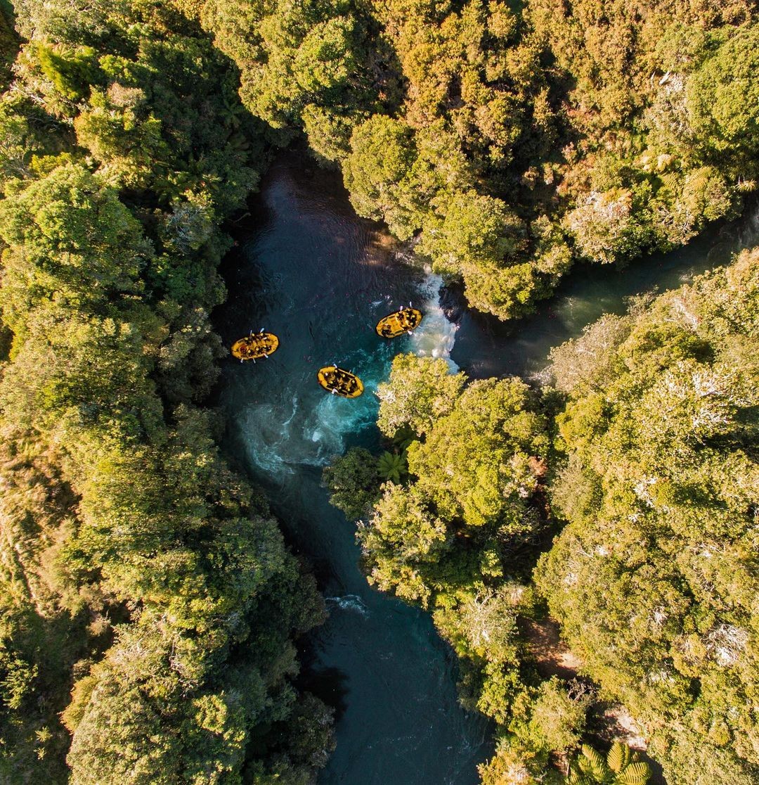 A group of customer on a Rotorua Rafting trip on the Kaituna River join paddles in the middle to celebrate navigating down a section of rapids.