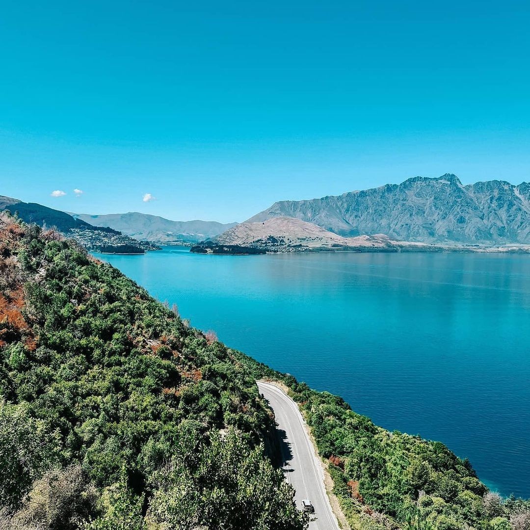 An aerial view of a scenic road in Queenstown hugging the shores of Lake Whakatipu.
