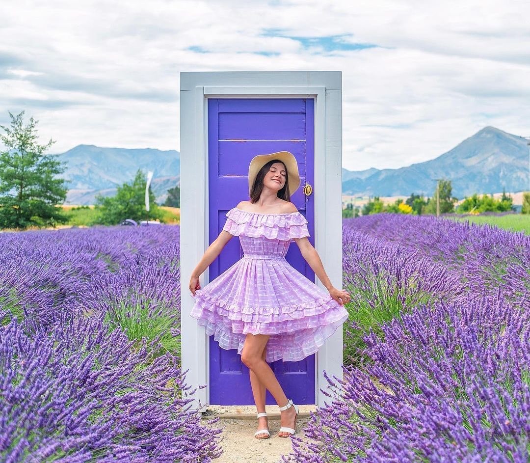 A woman poses in front of a purple door at the Wanaka Lavender Farm with lavender all around her.