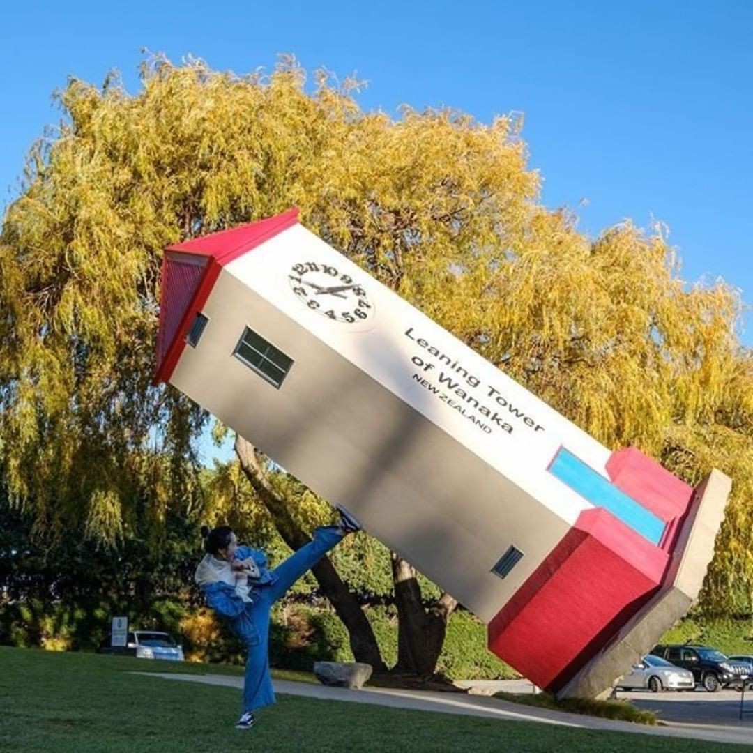 A man pretends to hold up a leaning tower with his leg at Puzzling World in Wanaka.