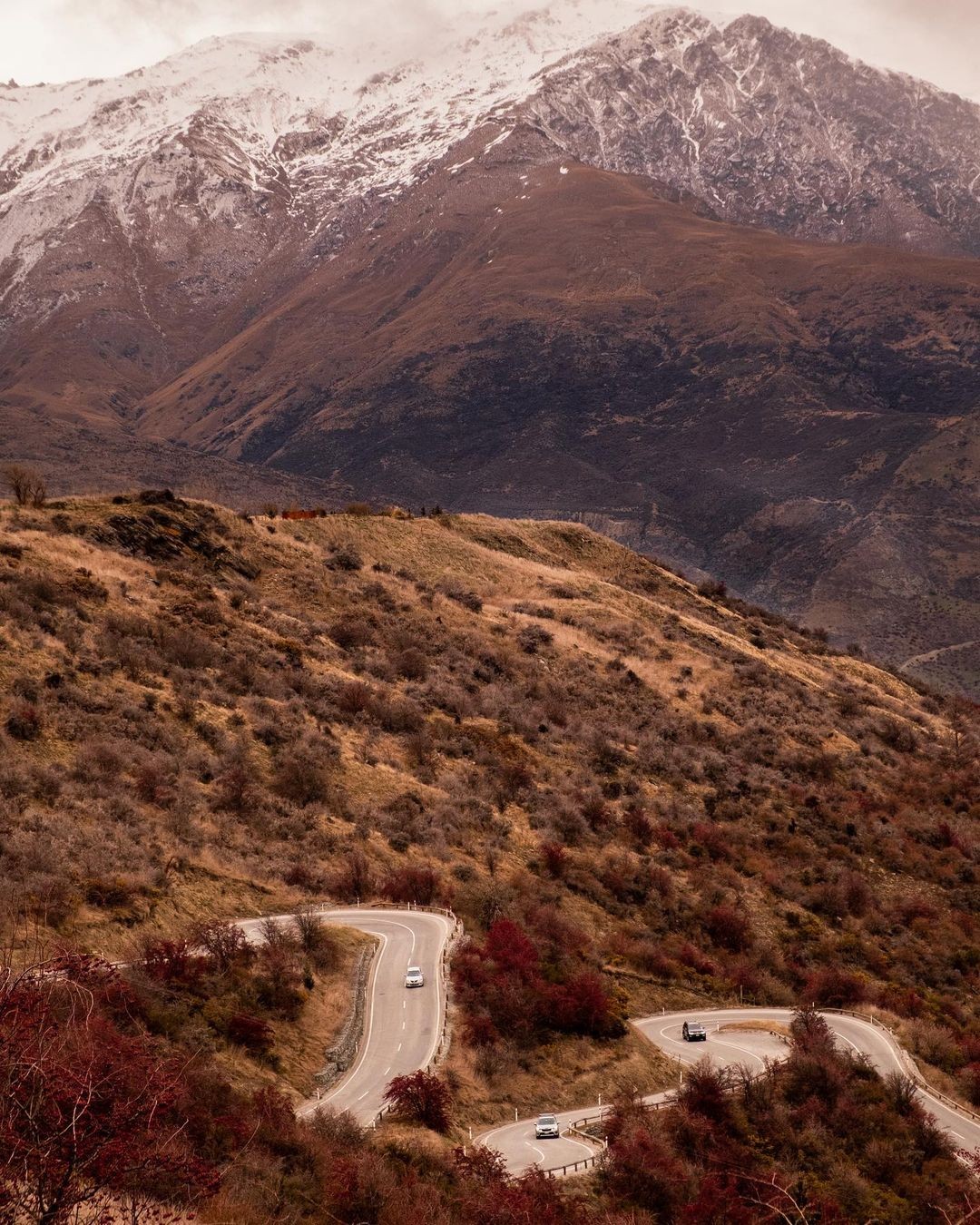 A stunning photo of the crown range road switchbacks with towering mountains behind.