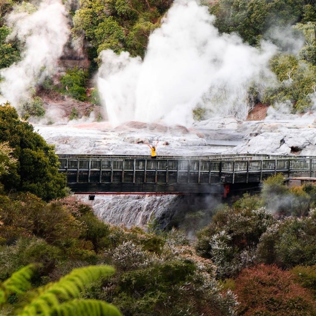 A person stands on a bridge and marvels at the Pōhutu Geyser erupting at Te Puia in Rotorua.