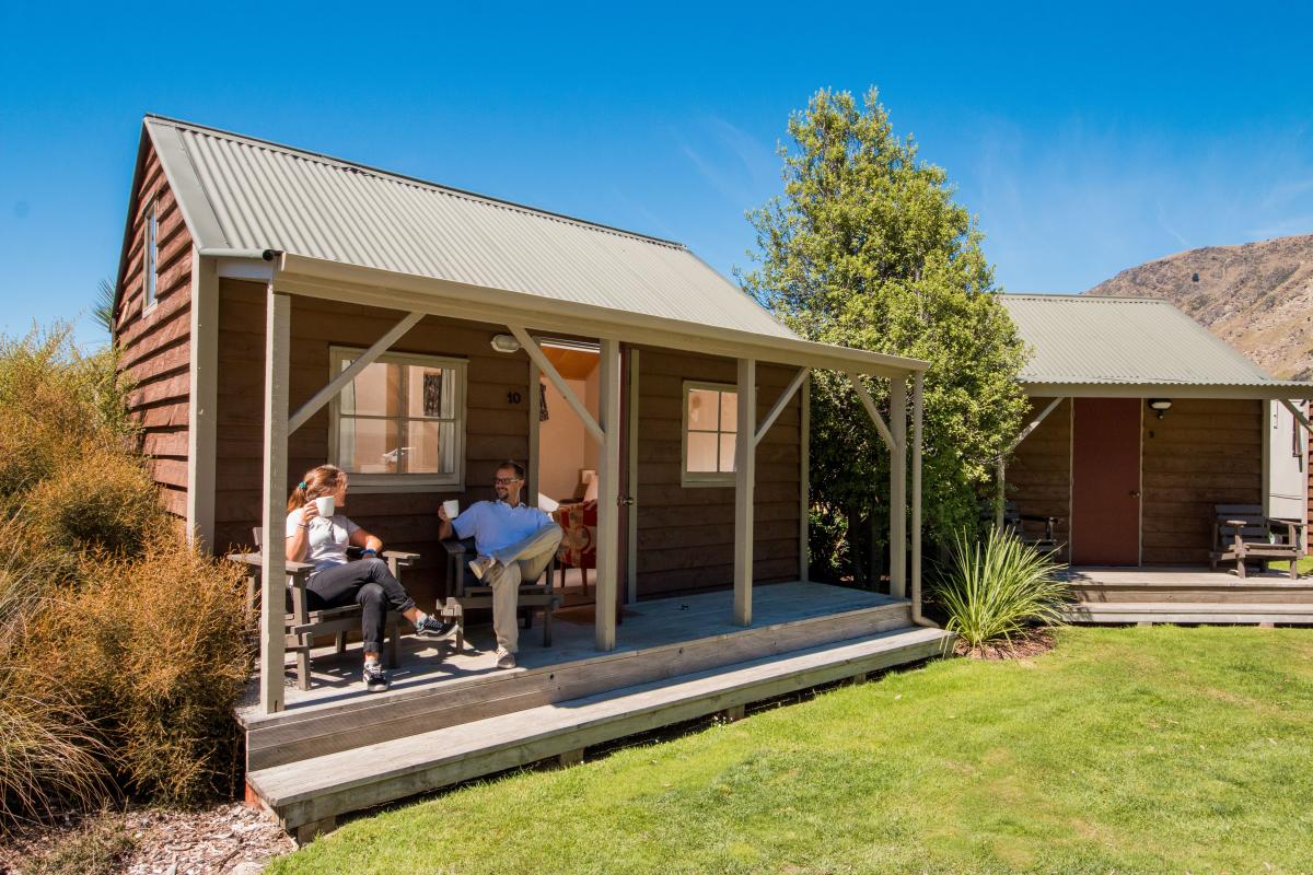 A couple sits outside on the deck of their 1 bedroom unit at the Top 10 Holiday Park in Arthurs Point, Queenstown.