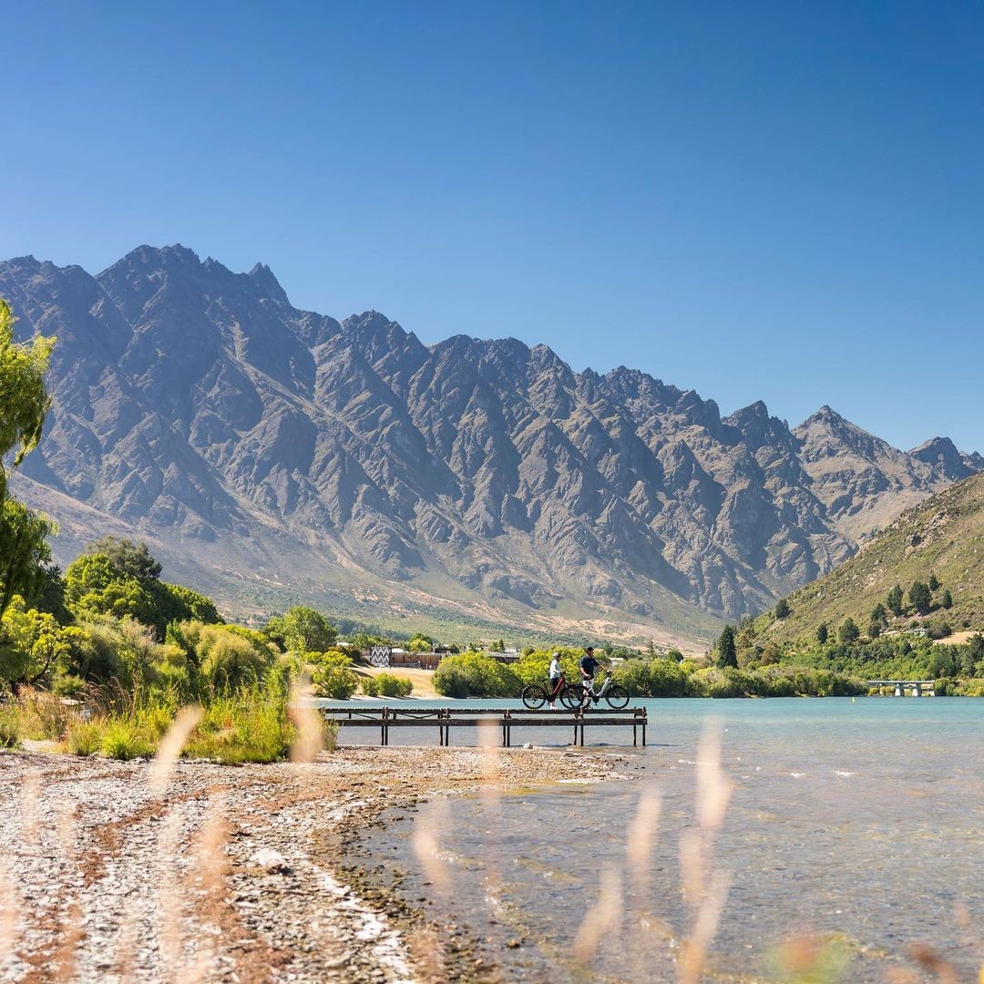 Two bikers stand on the end of a jetty in the Frankton Arm of Lake Wakatipu.
