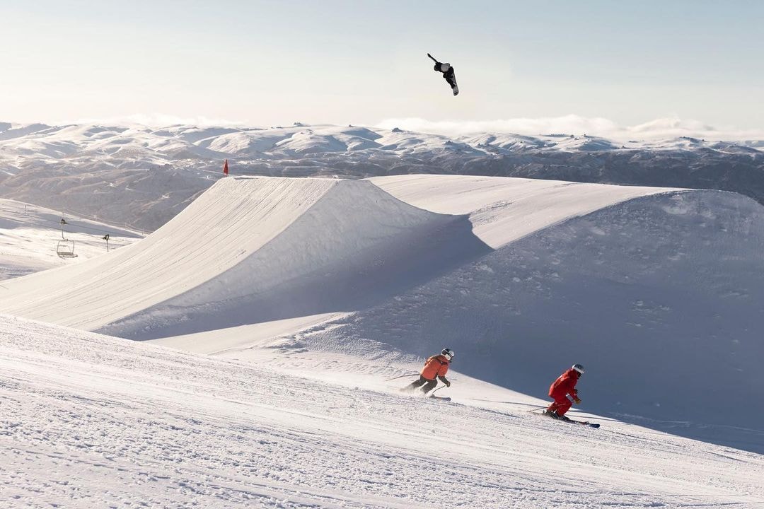 Tow skiers descend a slope at Cardrona as a Snow Boarder gets some serious air on a jump in the park.