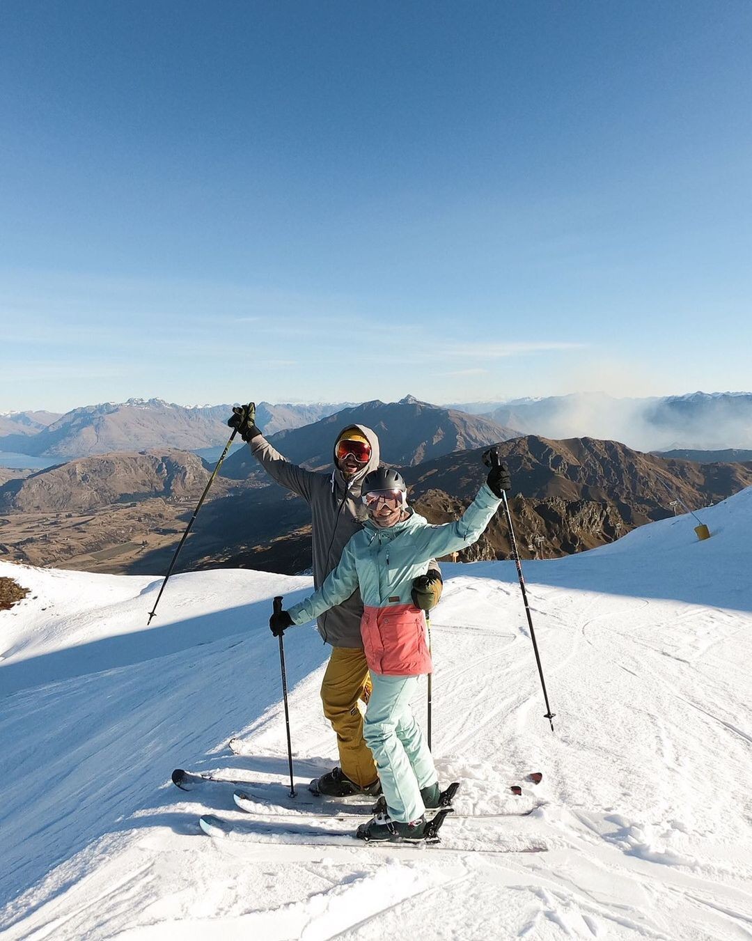 A couple raises there ski poles in the air ready to head down a ski run at Coronet Peak.