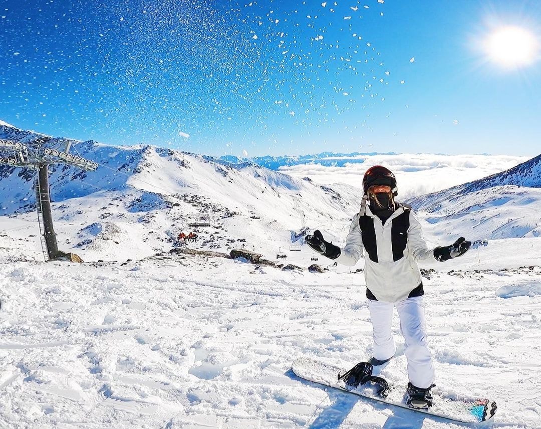 A girl throws some snow in the air above her whilst snow boarding at The Remarkables mountain.