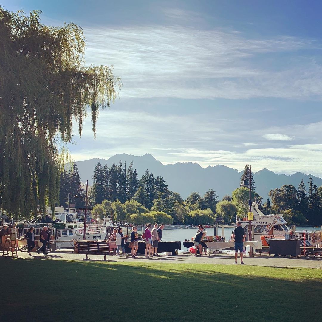 A group of people stop and look at a market stall at the Queenstown lakefront markets.