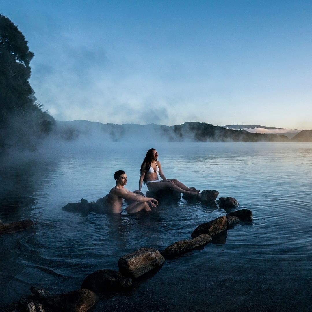 A couple relaxes and enjoys a sunset whilst bathing in the naturally heated waters of Hot Water Beach - Te Rātā Bay.