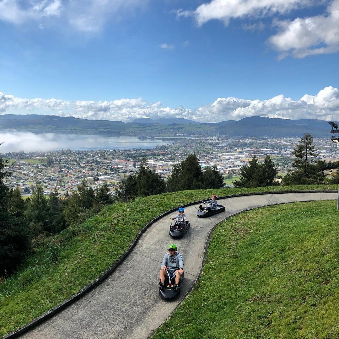 A family goes Luging at Skyline Rotorua with expansive views of the city and lake behind.