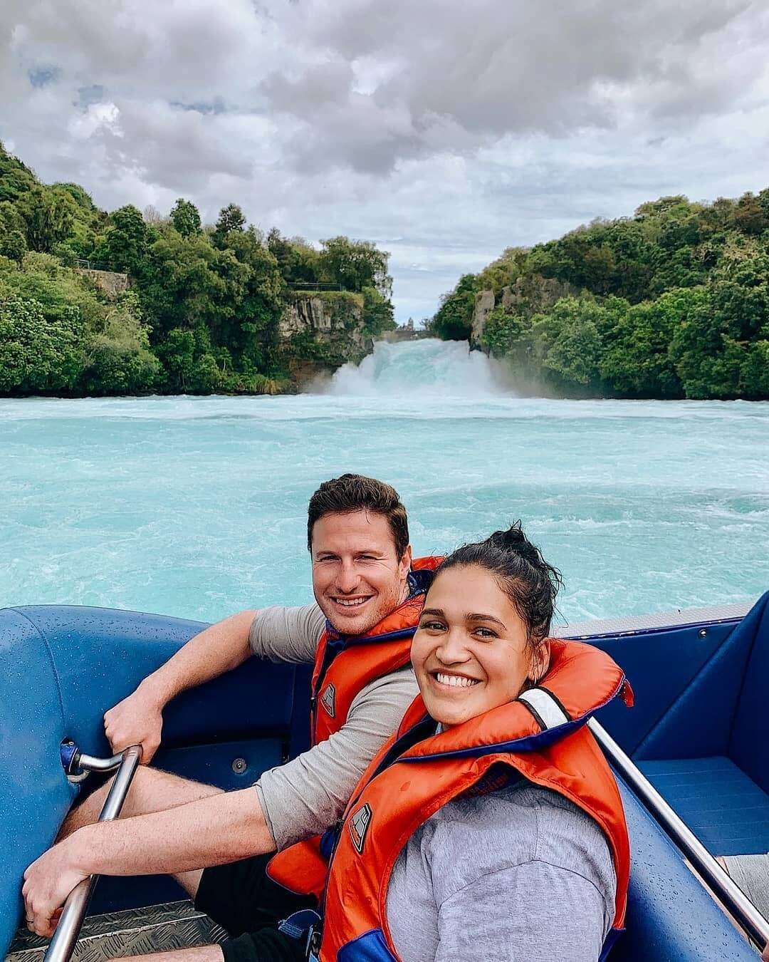 Couple enjoying a jetboat ride past the Huka falls, with the waterfall flowing in the background.