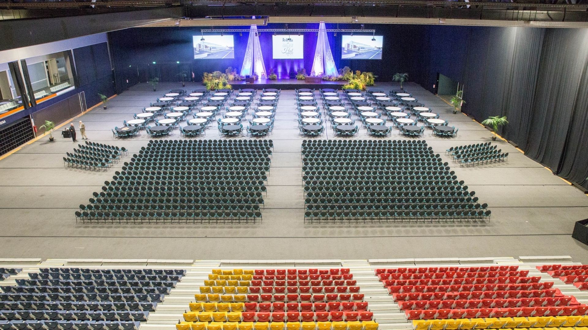 An empty Energy Events Centre prepares for a packed conference event with seats arranged facing three screens.