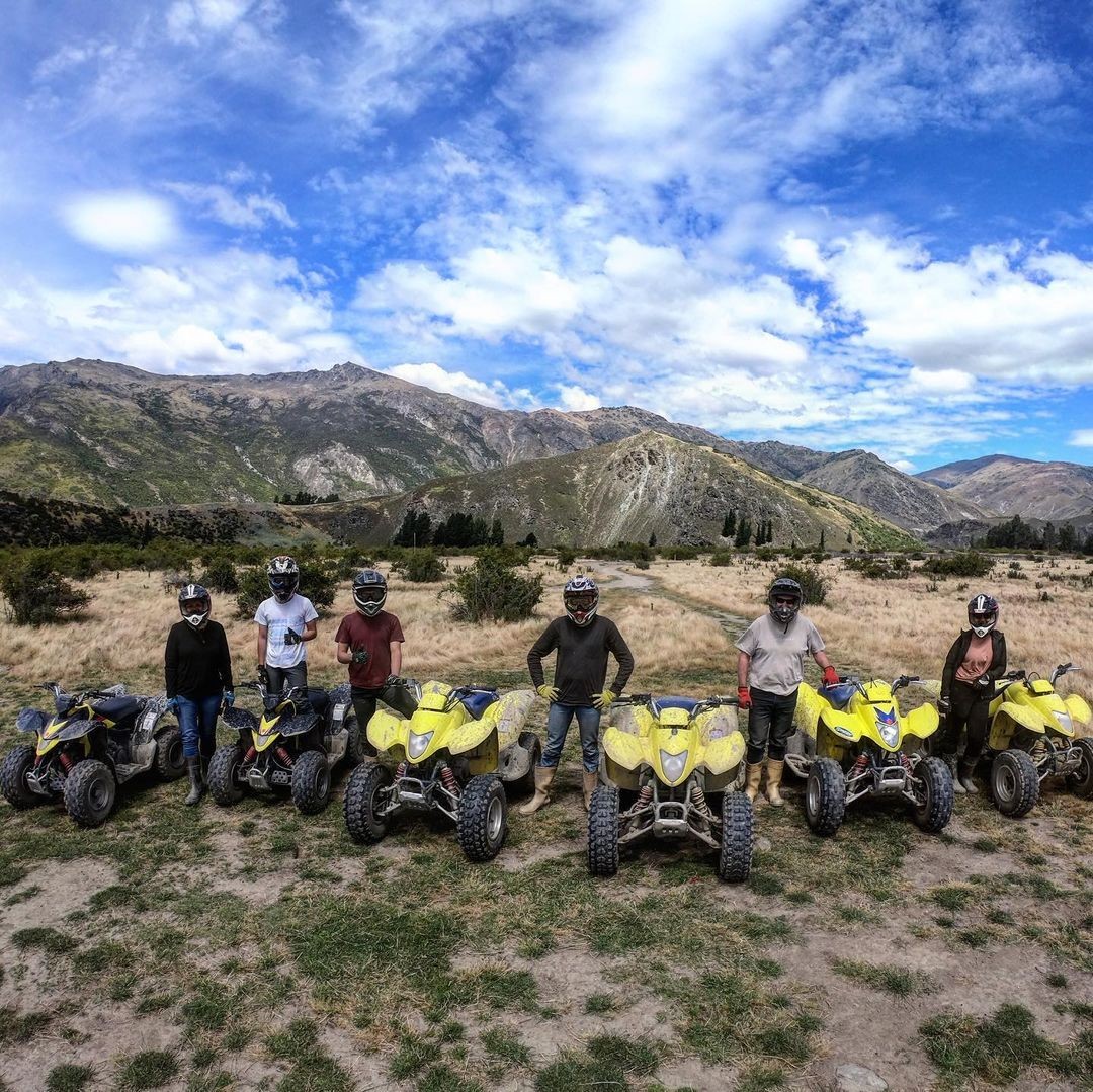 A group of friends pose for a photo in front of their quad bikes.