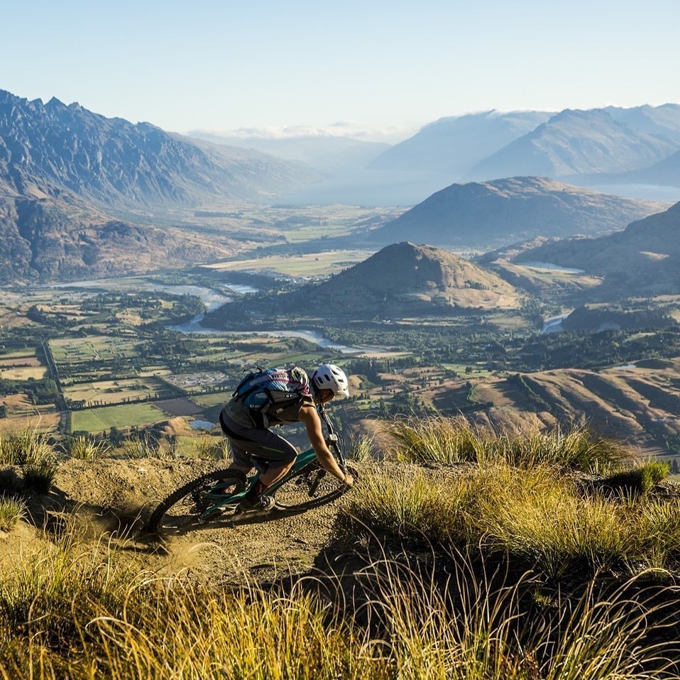 A person rides a downhill MTB track at Coronet Peak with incredible views in the background.