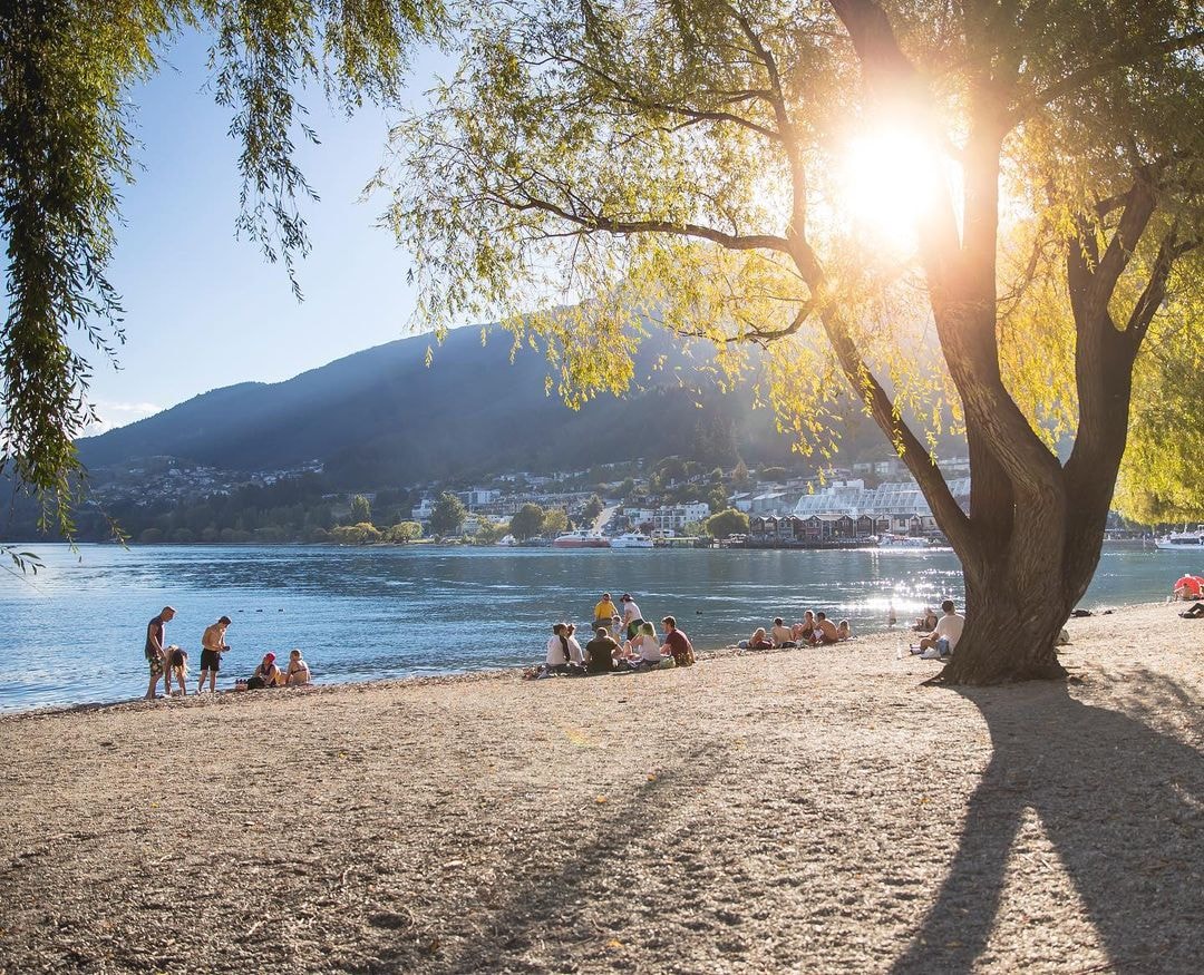 Groups of people sit and appreciate the stunning Queenstown lakefront as the sun sets.