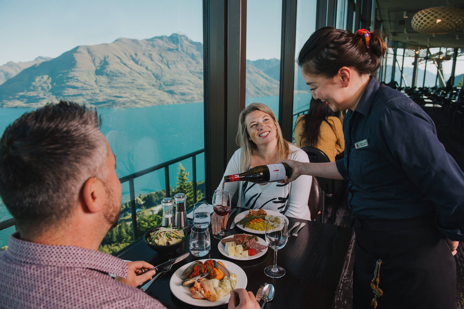 A waitress tops up a ladies glass with wine in the Stratosfare Restaurant at Skyline Queenstown.