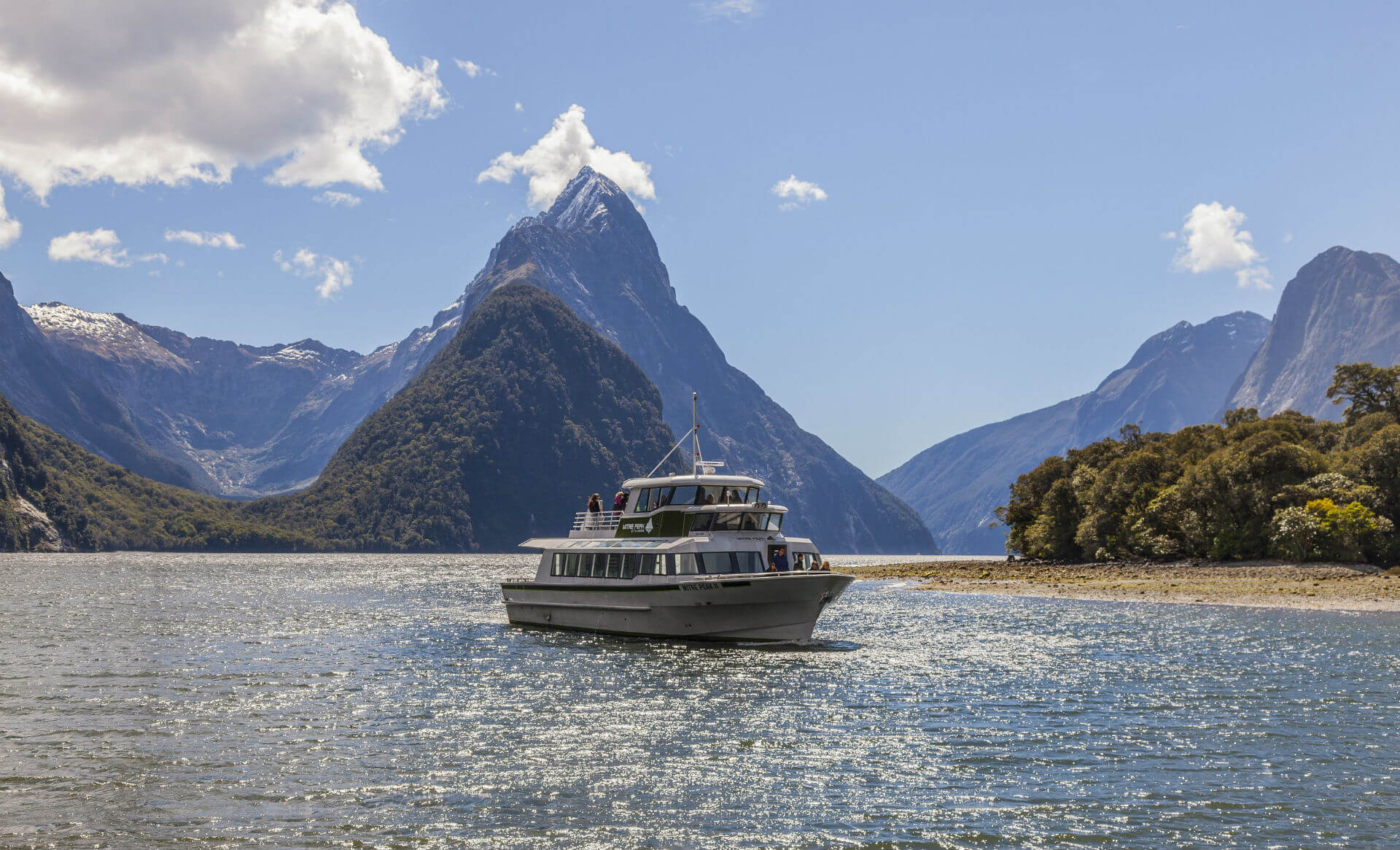 A Mitre Peak Cruises boat meanders through Milford Sound with tourist aboard.